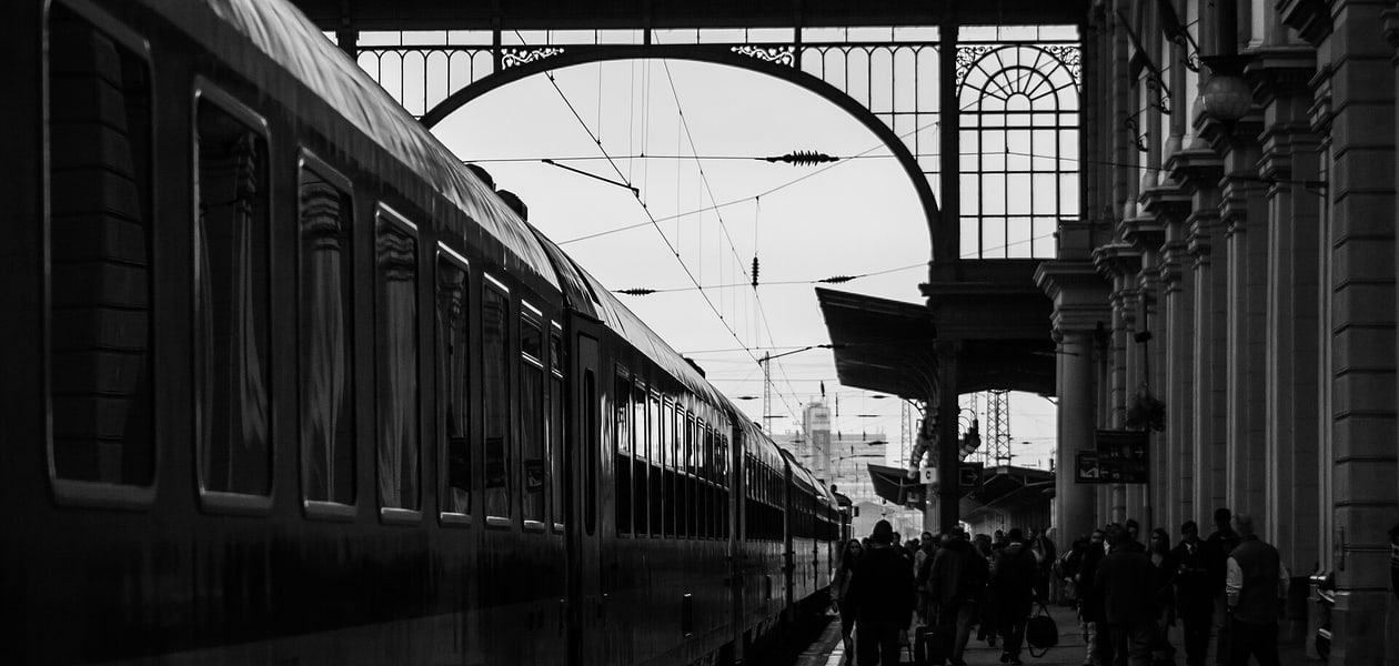Travellers on a station platform at dawn, seen through the great arched portal of Budapest Keleti